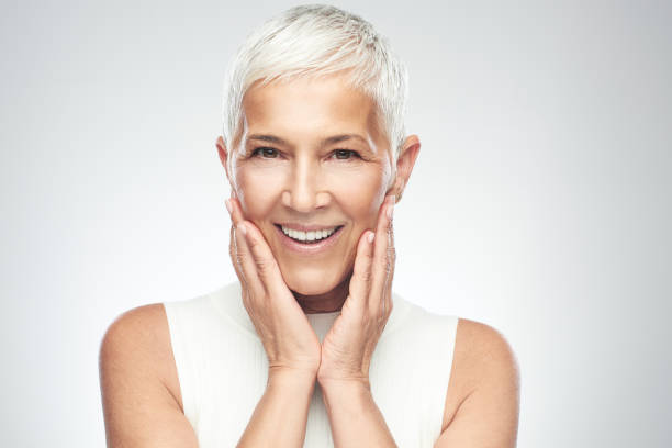 Beautiful smiling senior woman with short gray hair posing in front of gray background. Beauty photography.